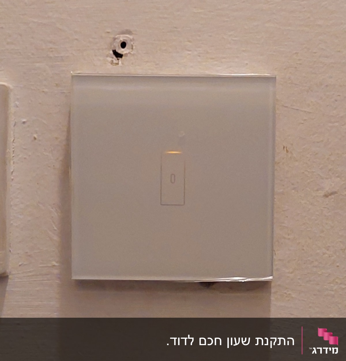מתג חשמלי על קיר לבן עם חור מעליו